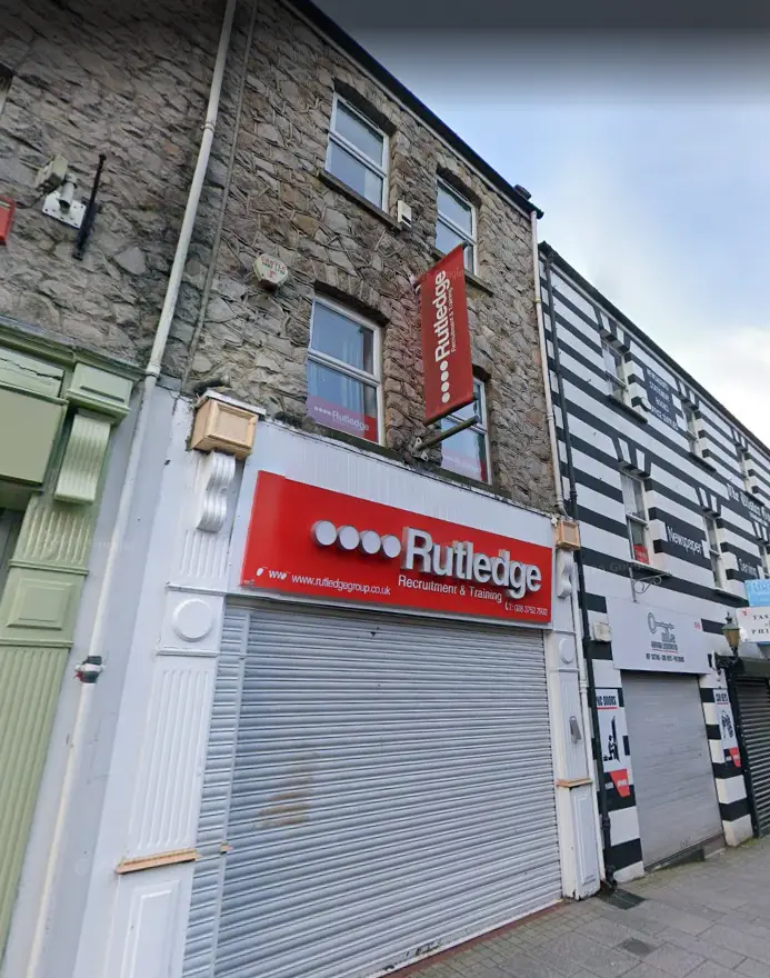 Rutledge Recruitment & Training Armagh branch, red shopfront with shutter beneath a stone terrace, with a vertical red Rutledge banner above.