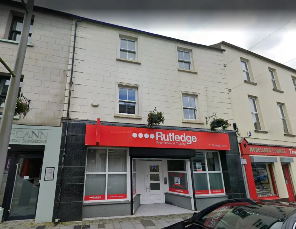 Rutledge Recruitment & Training Enniskillen branch, cream three-storey terrace with a bold red Rutledge shopfront, hanging flower baskets and central white entrance door.