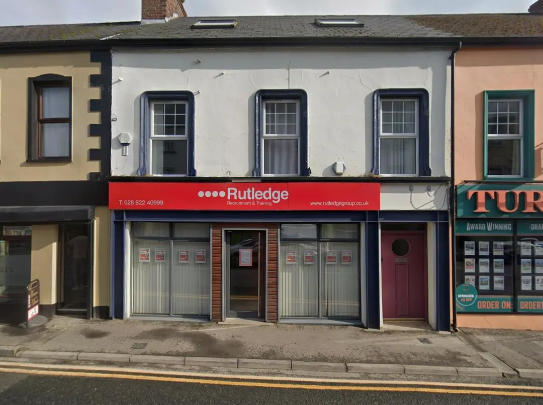 Rutledge Recruitment & Training Omagh branch, white rendered two-storey terrace with a bold red Rutledge shopfront and central recessed entrance.